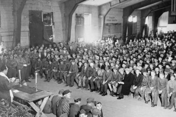 English: Rabbi Hershel Schaecter officiates at Shavuot services for Buchenwald survivors. Pictured in the audience are Robert Yehoshua Büchler (front row, shorts), Yisrael Meir Lau, and other notable individuals.